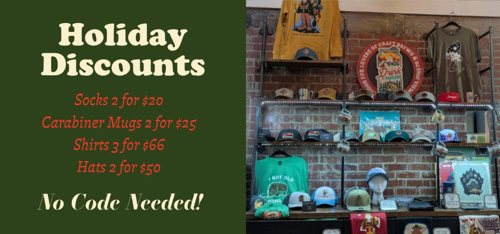 Promotional sign for holiday discounts on merchandise with a display of hats and shirts in the background.